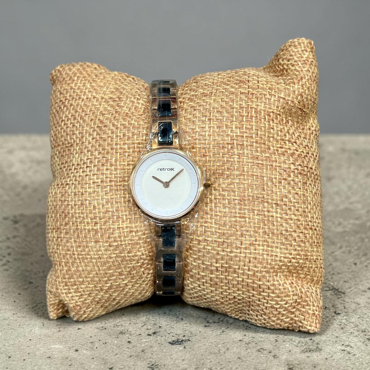 Retro X women's slim stainless steel watch with rose gold tone case, navy blue link bracelet and white dial, shown on a burlap pillow